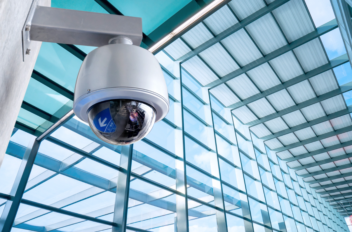 Dome-shaped CCTV camera hanging from wall in glass building