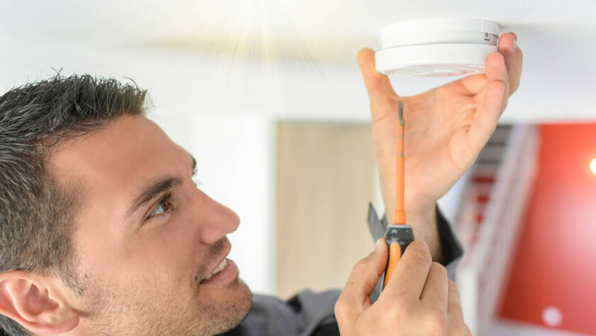 Male technician fits new fire alarm to replace old one